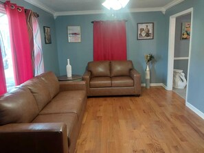 A living room with a brown leather sofa, a round side table, and a vase with dried flowers.