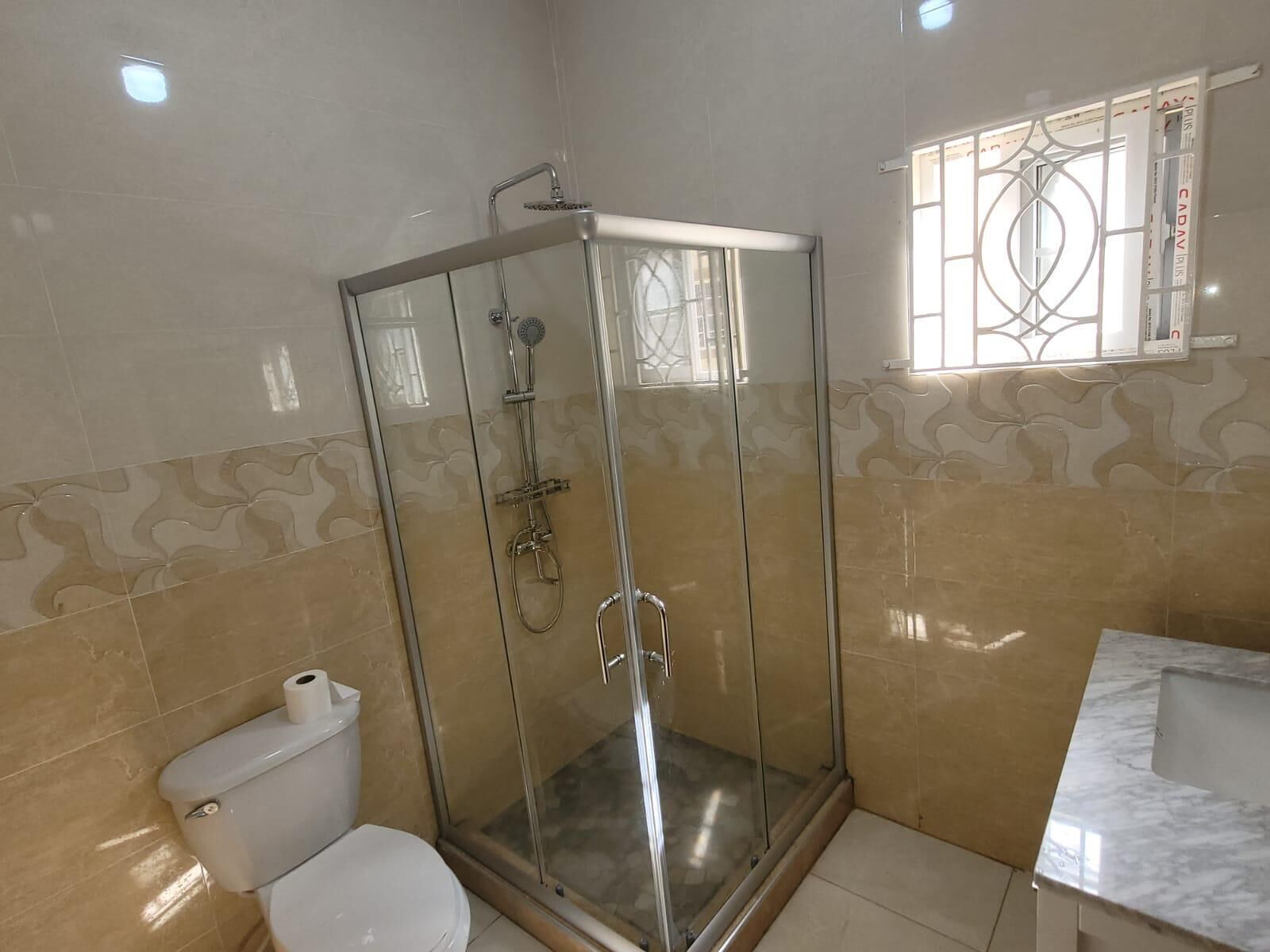 A bathroom with a glass-enclosed shower, a toilet, and a sink.