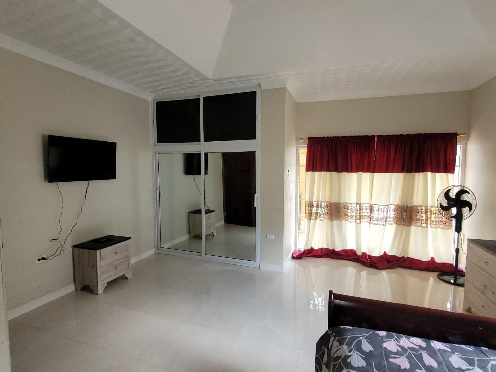 A bedroom with a TV, a sliding glass door, a bed, a dresser, and a fan.
