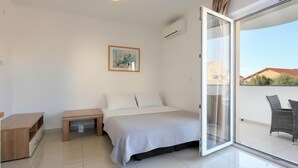 Una camera da letto con un letto, un comodino, un piccolo armadietto in legno, un quadro appeso alla parete e una porta scorrevole in vetro che dà su un balcone con mobili da esterno.
