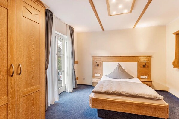 A bedroom with a wooden bed, a wardrobe, and a window with curtains. - Room 'Komfortzimmer' with Wi-Fi (Attendorn)