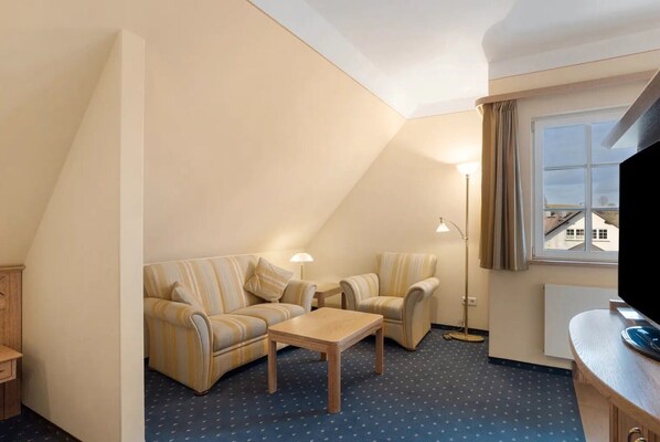 A small, cozy room with a sofa, two armchairs, a coffee table, a floor lamp, and a TV. - Room 'Luxury Room' with Wi-Fi (Attendorn)