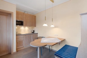 A compact kitchen with wooden cabinets, a microwave, and a dining area with a table and bench. - Room 'Luxury Room' with Wi-Fi (Attendorn)