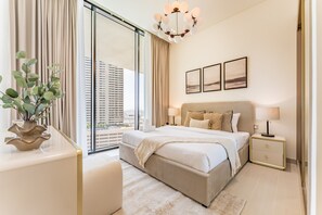 A modern bedroom with a large bed, bedside tables, a nightstand, a potted plant, and a view of the city through floor-to-ceiling windows. - Bright 1BR Apartment Stay with Mini Pool, Near Community Parks - Binghatti Royale, Jumeirah Village Circle (Dubai)