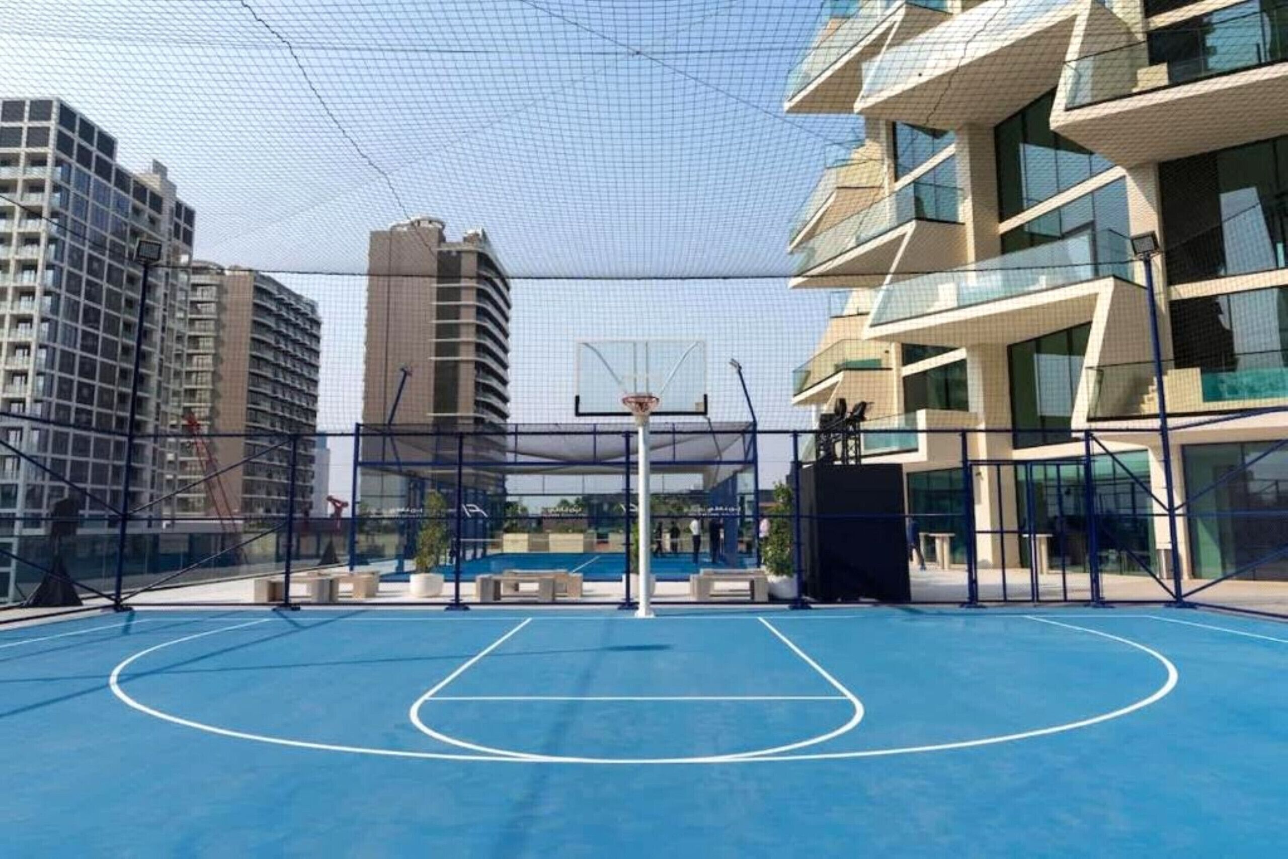 Een basketbalveld buiten met een net, omringd door moderne gebouwen.
