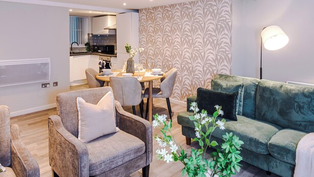 A spacious living area with a high ceiling, a dining table, and a green sofa. - Stylish 2 Bed 2 Bath Apartment – Liverpool Centre (Liverpool)