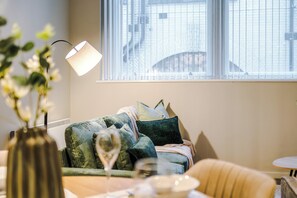 Un salon chaleureux avec un canapé, un vase rempli de fleurs et une table sur laquelle se trouve un verre.