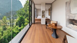 Een moderne hotelkamer met een ruim balkon, houten vloeren, een ronde eettafel en een schilderij aan de muur.