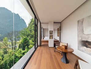 A modern hotel room with a large balcony, wooden flooring, a round dining table, and a painting on the wall. - Hidden Valley Hotel (Guilin)