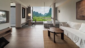 Een moderne woonkamer met een groot raam, een flatscreen televisie, een houten salontafel en een witte bank.