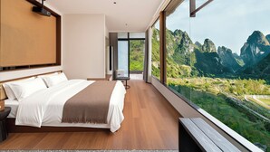Een moderne slaapkamer met een groot bed, een bankje en uitzicht op een bergachtig landschap.