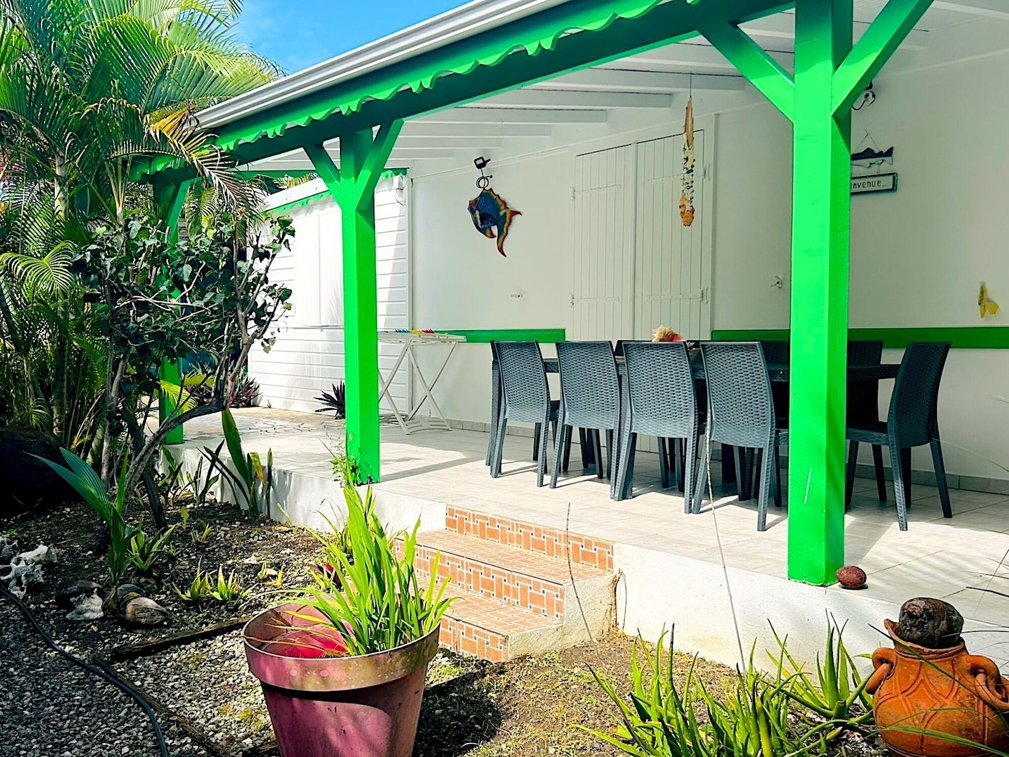 A covered patio area with a table and chairs, surrounded by potted plants and a brick pathway.