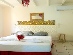 Una habitación de hotel con cama, cabecera decorativa, espejo y equipo de aire acondicionado.
