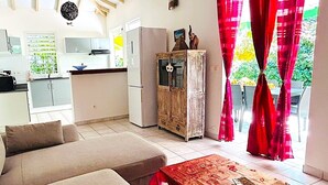 Una sala de estar acogedora con un sofá y una mesa de centro de madera, una cocina con armarios blancos y un refrigerador, y un comedor con cortinas rojas.