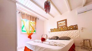 Un dormitorio con cama, una ventana con cortinas, un candelabro, un espejo y un taburete pequeño.