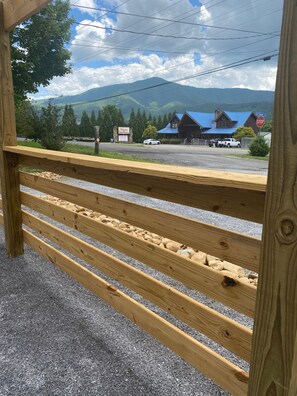 A wooden fence with a gravel path, a stop sign, a building with a blue roof, and a mountain in the background. - Mountain Laurel | King Suite for 2 | Wears Valley (Sevierville)