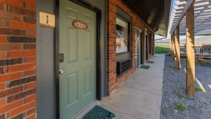 A building with a green door, brick walls, and a covered outdoor area with benches.