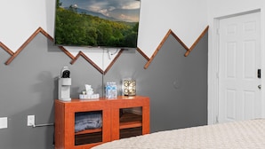 A bedroom with a bed, a TV mounted on the wall, a wooden nightstand with a lamp, and a white door.