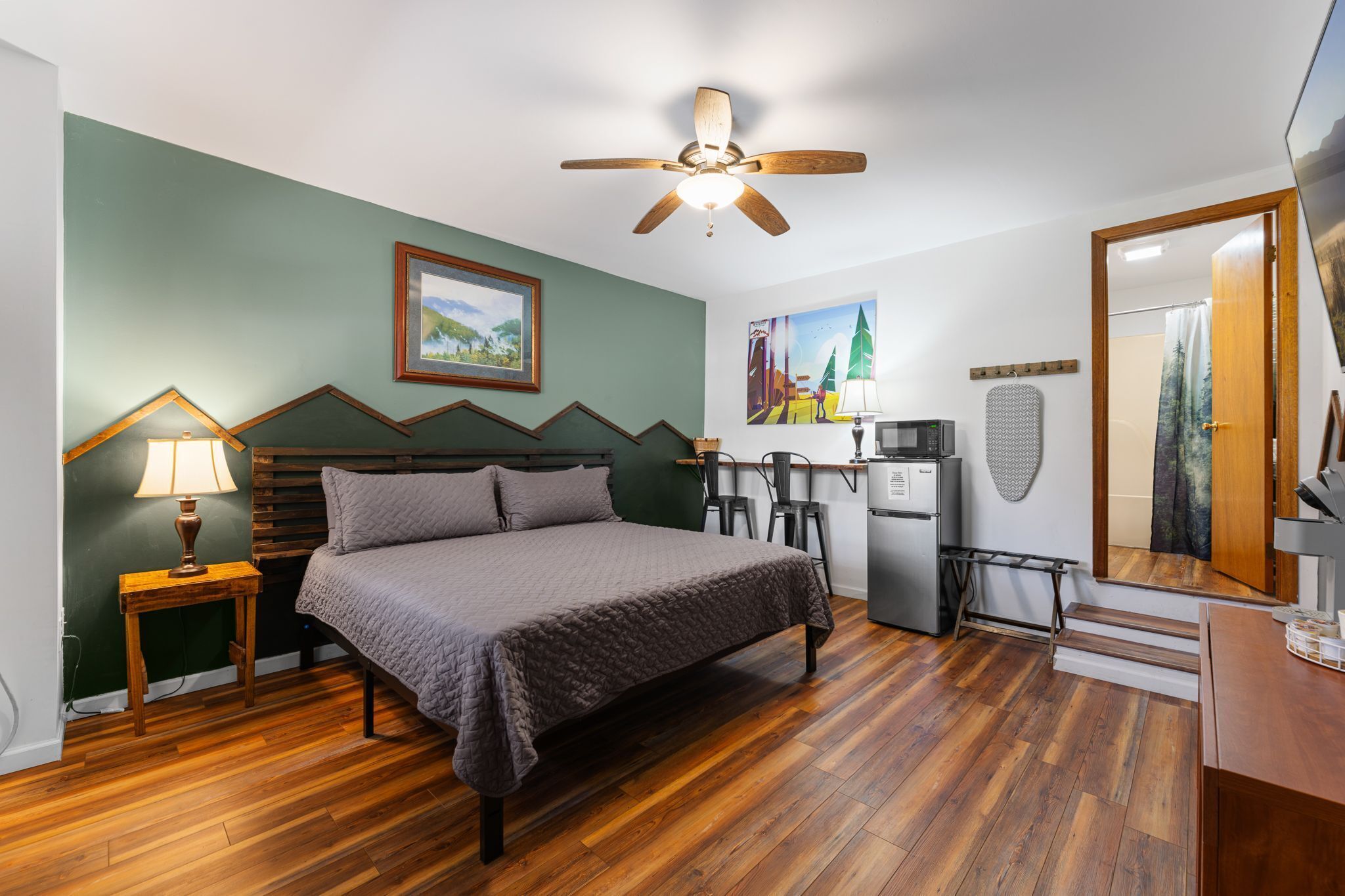 Une chambre à coucher comprenant un lit, un bureau, un réfrigérateur, un four à micro-ondes, un ventilateur de plafond, un tableau et une porte.