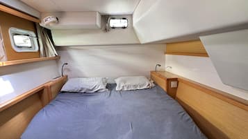 Un espacio interior compacto y bien iluminado, con una cama individual, un ventanal pequeño y un compartimento de almacenamiento.