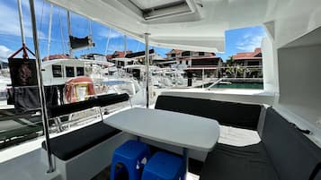 Interior de un barco con mesa, asientos y vistas al puerto deportivo.