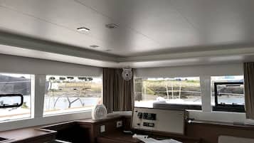 Una cabaña con un panel de control, ventanas que ofrecen vistas al exterior y una pequeña mesa con papeles.