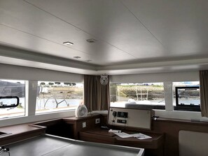 A cabin with a control panel, windows with views of the outside, and a small table with papers.