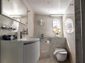 A modern bathroom with a curved vanity, a toilet, a shower area, and a large mirror.