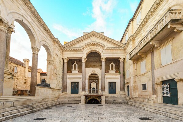 An open courtyard with classical architecture, including arches and columns, and a statue.