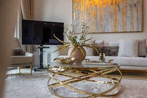Un salon moderne avec une table basse ronde en verre, un téléviseur à écran plat et un grand tableau abstrait accroché au mur.