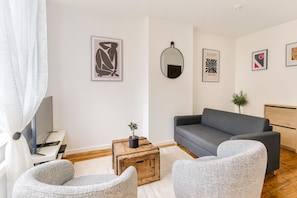 A modern living room with a grey sofa, two armchairs, a wooden coffee table with a plant, a flat-screen TV, and artwork on the walls. - Comfortable apartment! Quiet stay near Lille (Villeneuve-d'Ascq)