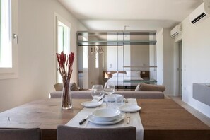 A modern dining area with a wooden table set for four, a vase with red flowers, and a glass partition separating the dining area from the living space. - Ca' Allegra  (Mogliano Veneto)