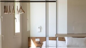 Et moderne hotelværelse med glasvæg, seng, sengebord og et siddeområde med et bord dækket til spisning.