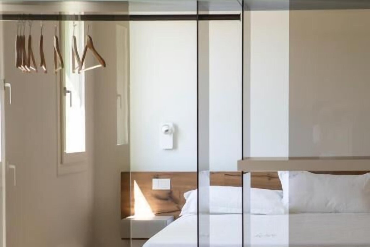 Une chambre d’hôtel moderne dotée d’une cloison en verre, d’un lit, d’une table de chevet et d’un coin salon avec une table dressée pour le repas.