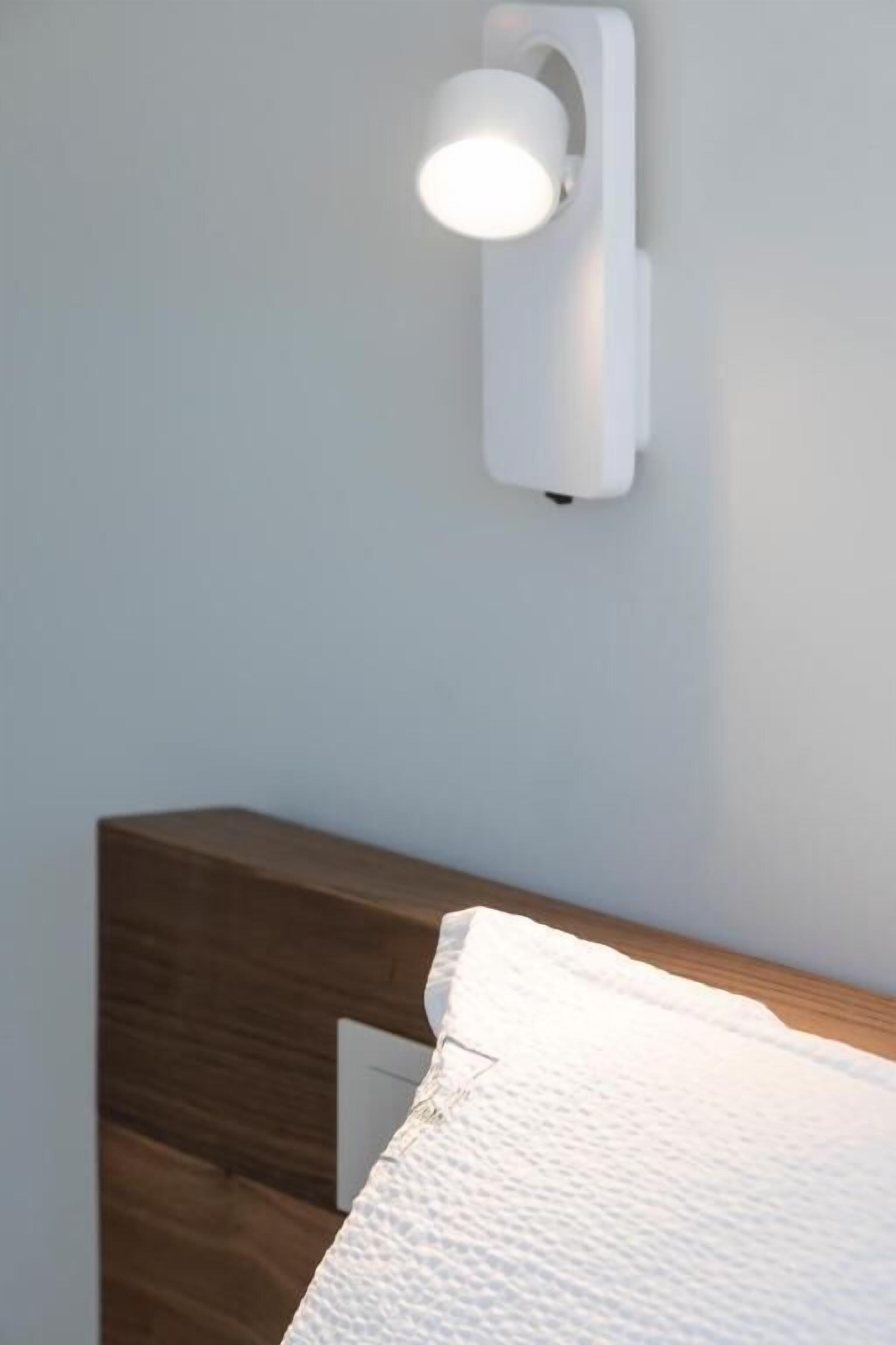 A bed with a white textured cover, a wooden headboard, and a wall-mounted light fixture.