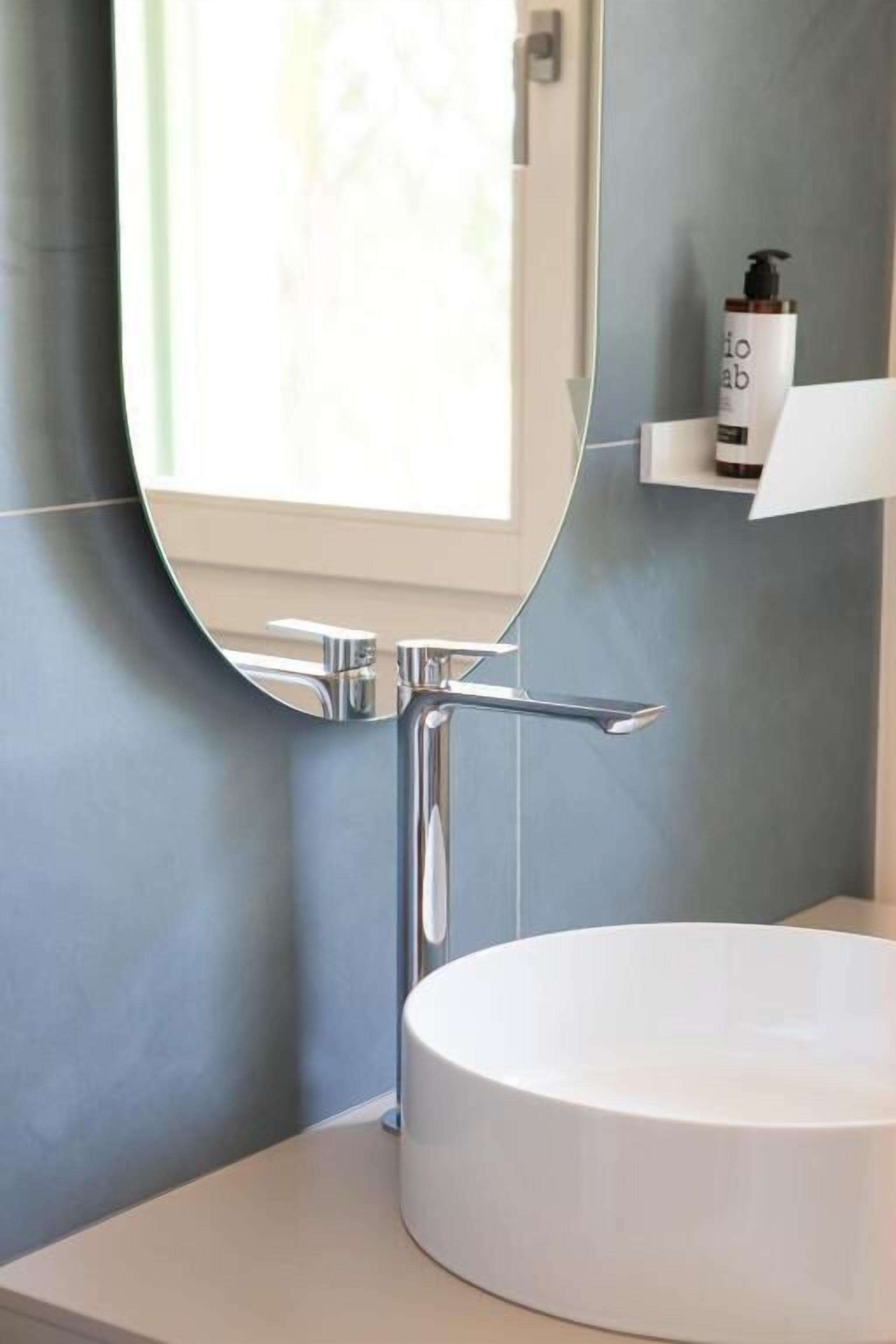 Un bagno con un lavandino rotondo bianco, un rubinetto cromato e uno specchio sopra.