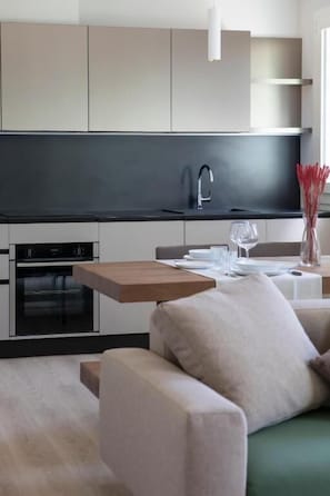 Una cocina moderna con electrodomésticos integrados, una zona de comedor con mesa de madera y un sofá.
