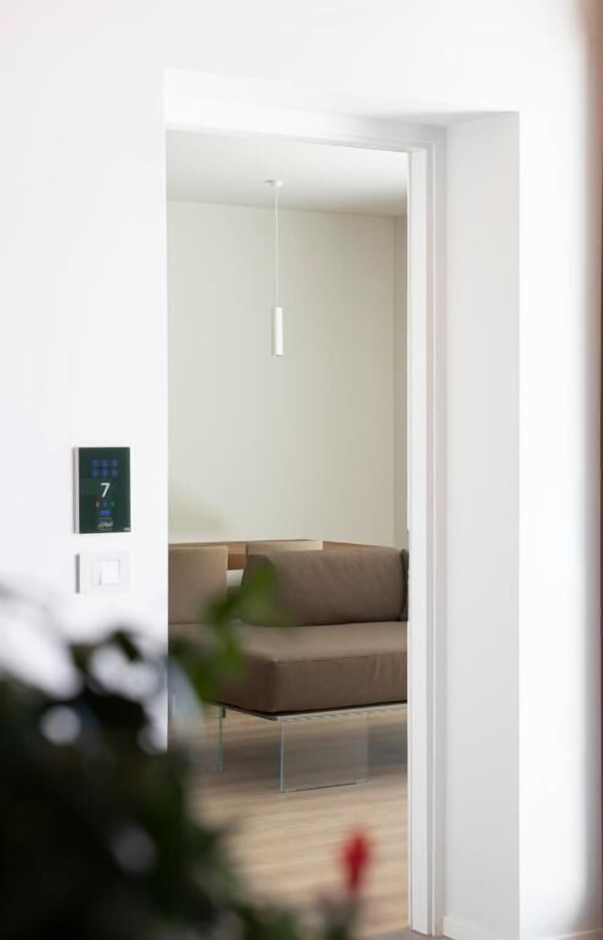 Una habitación moderna con diseño minimalista, que incluye un sofá, un panel de control en la pared y una lámpara colgante.