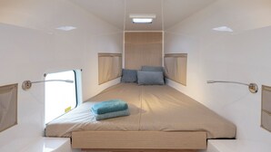 A narrow, elongated room with a bed at the center, a window on one side, and a shower area on the other.
