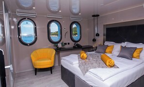 A modern bedroom with a bed, a yellow armchair, and three round windows with views of the sea. - Sun-Kissed Sailing Adventure in Split, Croatia (Split)