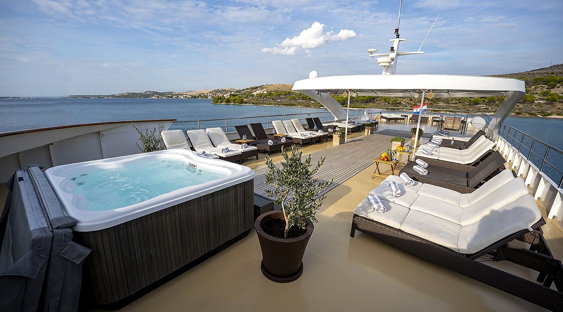 A deck with a hot tub, lounge chairs, and a potted plant.