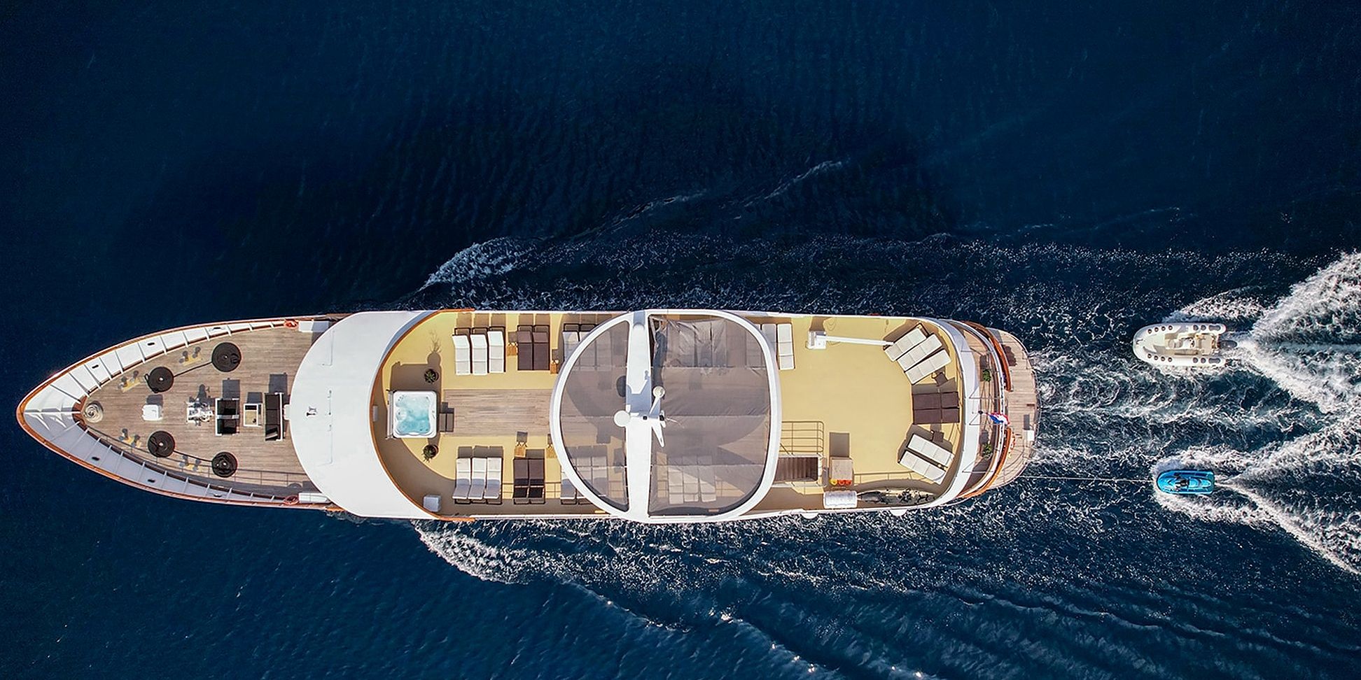 An aerial view of a yacht with a sun deck, lounge areas, and a hot tub.