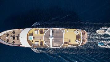 An aerial view of a yacht with a sun deck, lounge areas, and a hot tub.
