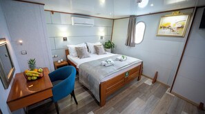 Ett hotellrum med en säng, ett skrivbord med en fruktskål, en stol, en krukväxt och en tavla på väggen.