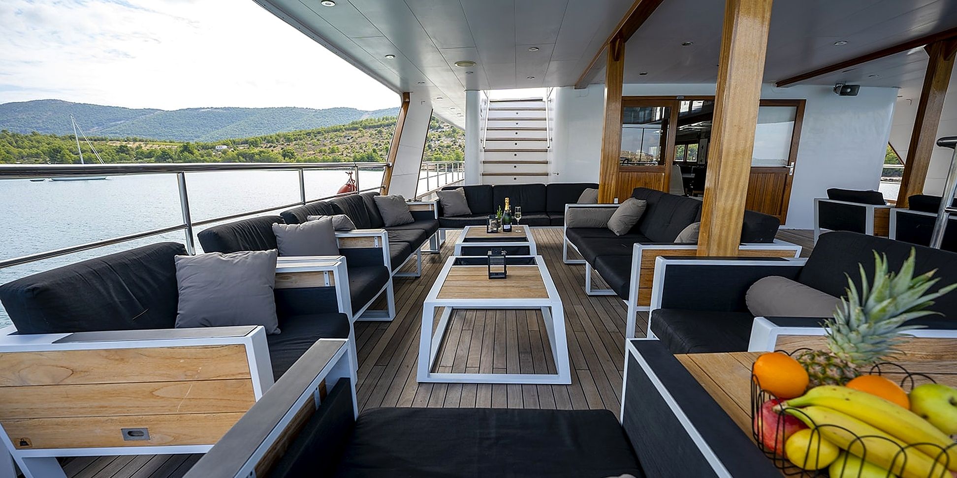 A deck with outdoor seating, a table with drinks, and a view of the water.