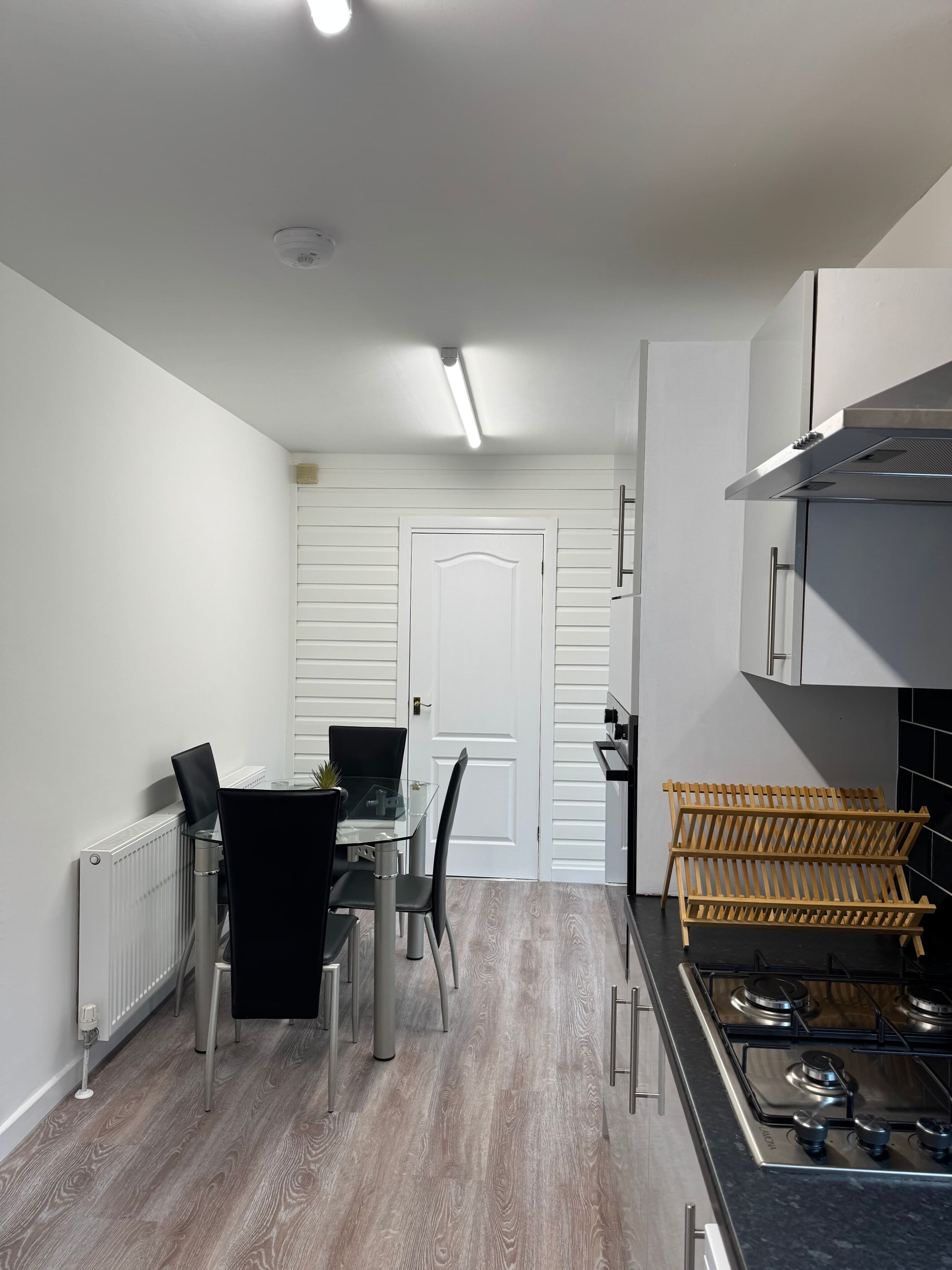Uma cozinha compacta com mesa, cadeiras, fogão e uma porta branca.