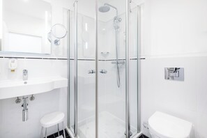 Een moderne badkamer met een douchecabine van glas, een witte wastafel en een toilet.