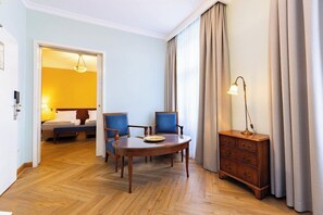 Een hotelkamer met een houten vloer, een rond tafeltje met stoelen, een nachtkastje met een lamp en een kledingkast.