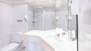 Un baño moderno con un inodoro blanco, un lavabo con espejo y una zona de ducha.