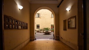 A hallway with an arched entrance, a row of framed items on the left wall, and a potted plant in the center. - GuestHost - A practical and welcoming 50 square meters open-plan loft, perfect for two people, located on the ground floor of an elegant building with a courtyard.The property is located in the Prati district, one of Rome's most charming areas: our guest (Rome)